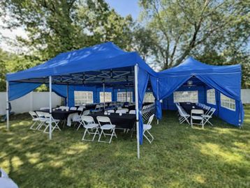 Blue event tents set up on a grassy lawn with white folding chairs inside.