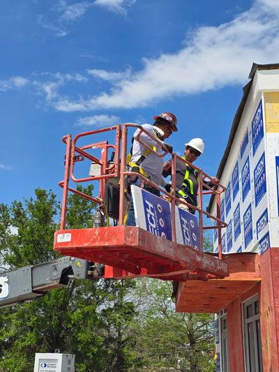 Two construction workers on a red lift working on a building exterior.