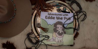 A children's book titled 'Adventures with Eddie the Pug' placed on a fur surface.