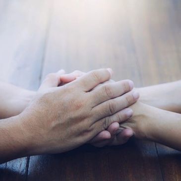 Two people holding hands on a wooden surface, symbolizing support and connection.