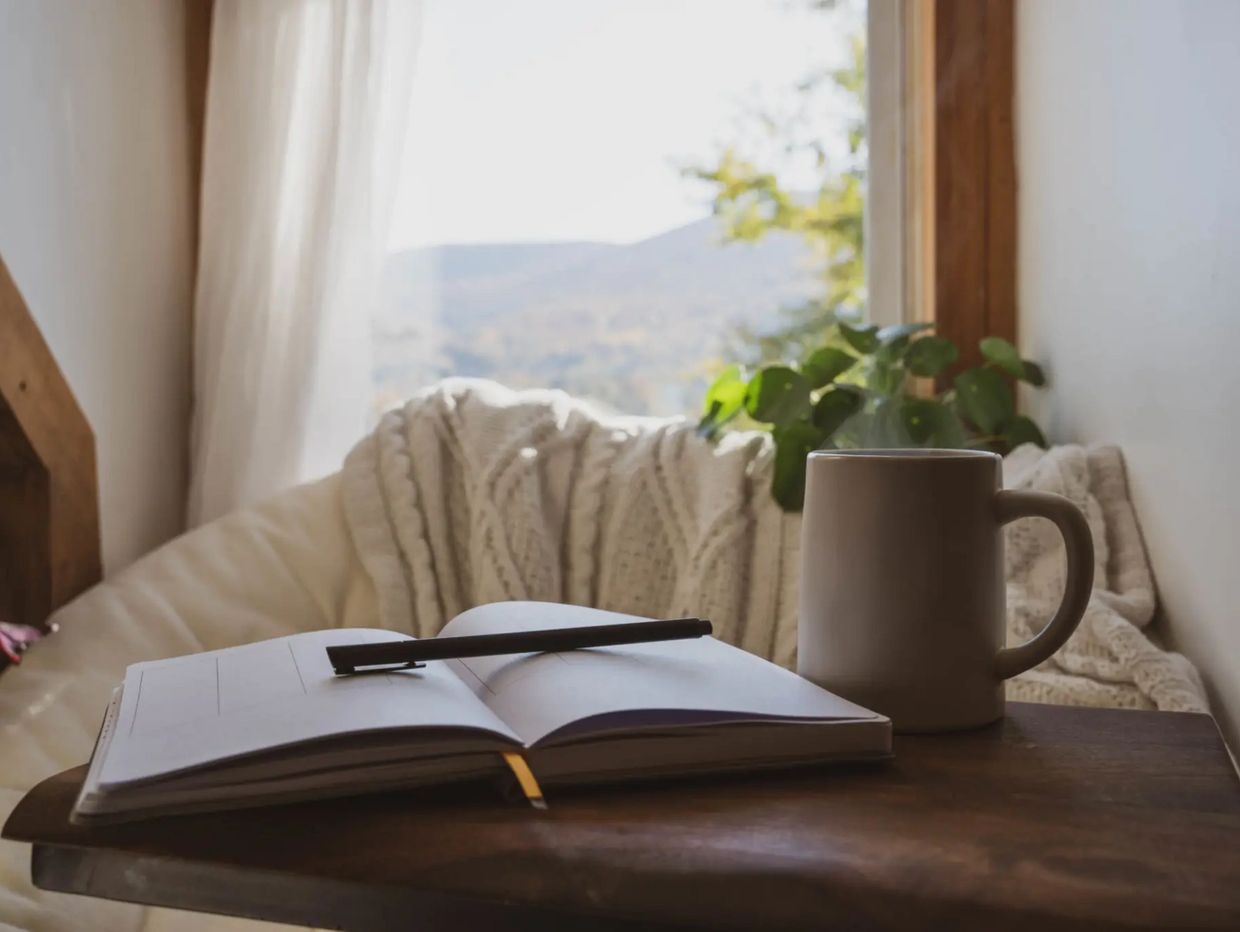 Cozy nook with a journal, pen, and steaming mug by a sunlit window.