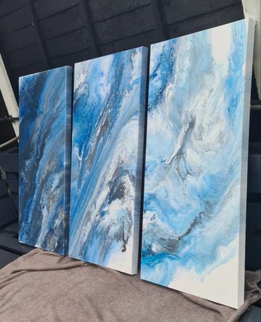 Three abstract blue and white fluid art paintings displayed together.
