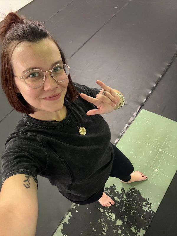 Smiling woman on a yoga mat making a hand sign.