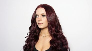 Woman with long wavy burgundy hair looks to the side.