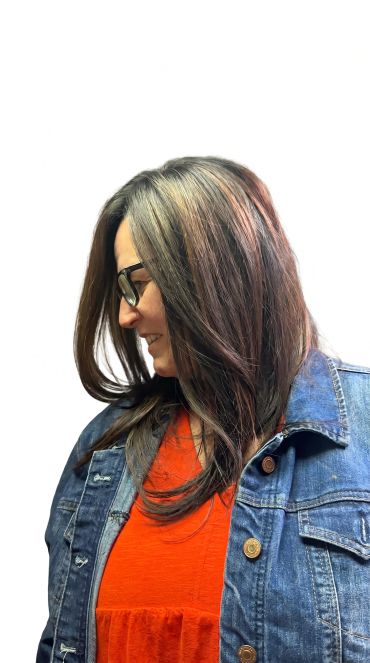 Smiling woman with brown hair wearing glasses and denim jacket.