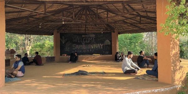 People sitting in pairs under a rustic shelter with a welcome sign on the blackboard.
