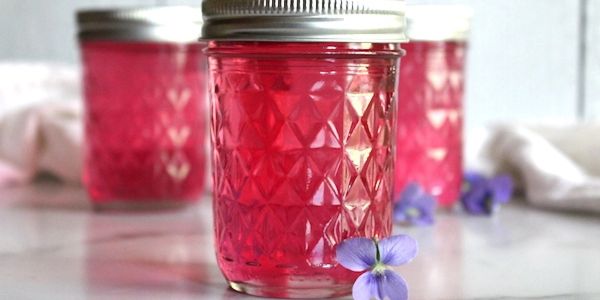 Jars filled with vibrant red jelly, adorned with small purple flowers.