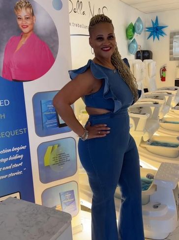 Woman in blue jumpsuit poses confidently in a modern salon setting.
