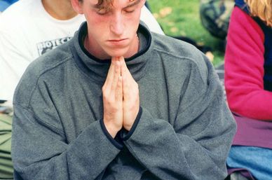 Young man praying with hands together and eyes closed.