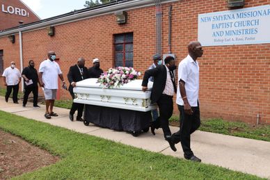 Men carrying a white casket adorned with flowers at a church funeral.