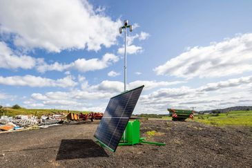 Solar panel and weather station setup in a rural field under a blue sky.