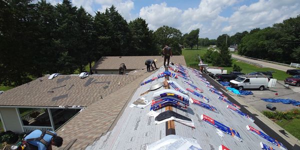 Roofers installing new shingles on a house roof under a sunny sky.