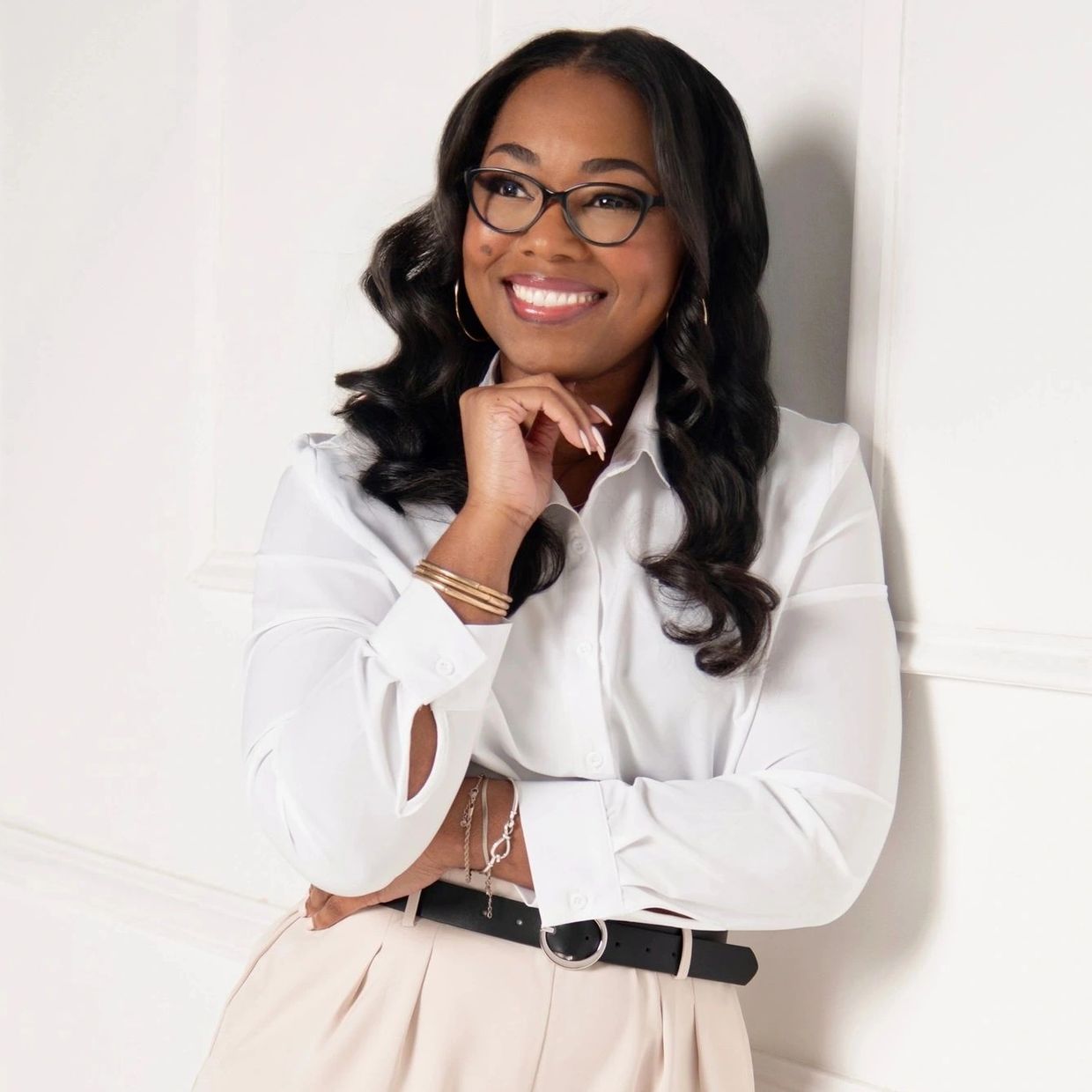 Smiling woman in glasses and stylish white shirt with beige pants.