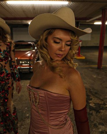 Woman in a cowboy hat and elegant dress in a dim garage.