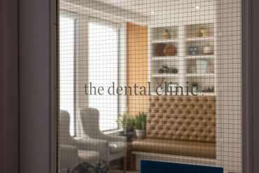 View through a glass door into a cozy dental clinic waiting area with chairs and plants.