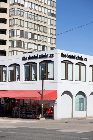 A white building with a dental clinic sign and a red awning on a sunny day.