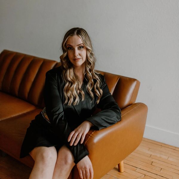 Woman with wavy blonde hair sitting on a brown leather couch.