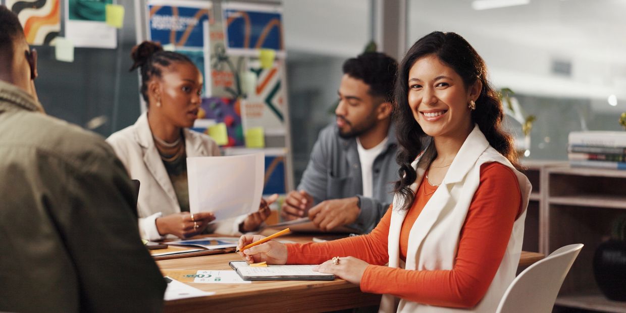 Young woman smiling confidently during a group meeting in a modern office.