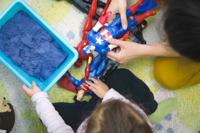 Children playing with superhero action figures and kinetic sand.