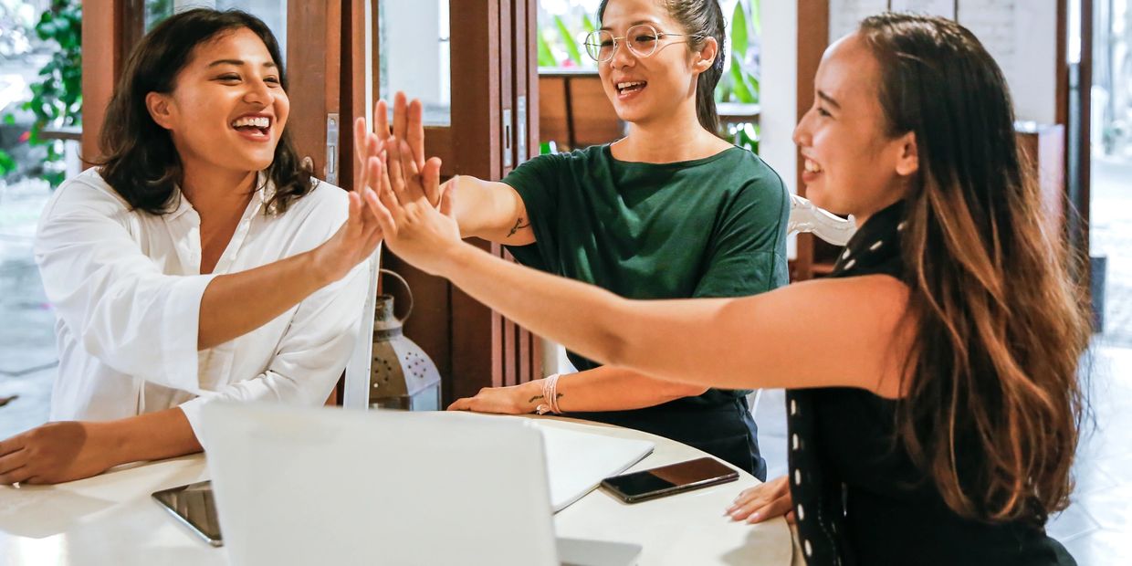 Three women high-five in front of a laptop