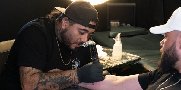 Tattoo artist concentrating while tattooing a client's forearm in a studio.