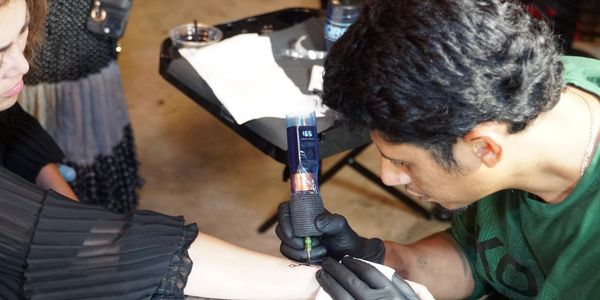 A tattoo artist carefully inks a woman's forearm in a studio.