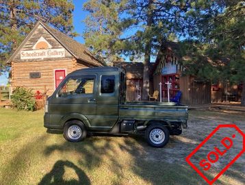 A small black pickup truck parked near a wooden gallery with a 'SOLD' stamp.