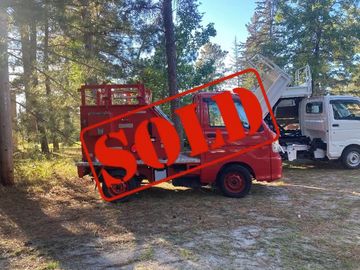 Red utility truck with a SOLD sign in a forested area.