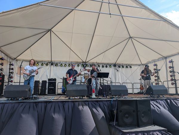 Band performing live on an outdoor stage under a large tent.
