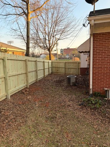New wooden fence alongside a brick house with fallen leaves on the ground.