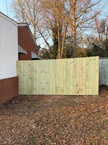 Newly installed wooden fence against a brick building and trees.