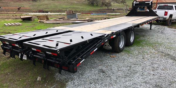 A flatbed trailer attached to a white pickup truck in a rural setting.