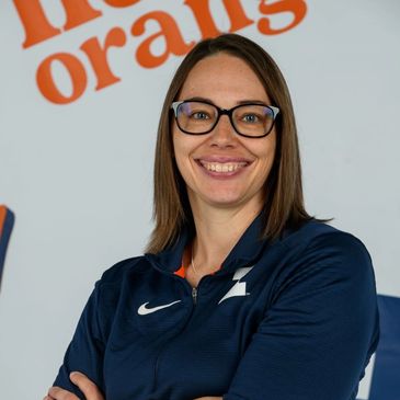 A head shot of a white woman wearing a navy blue polo and black-rimmed glasses and smiling