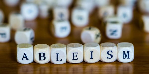 "Ableism" spelled out in individual letters on dice with other dice in the background