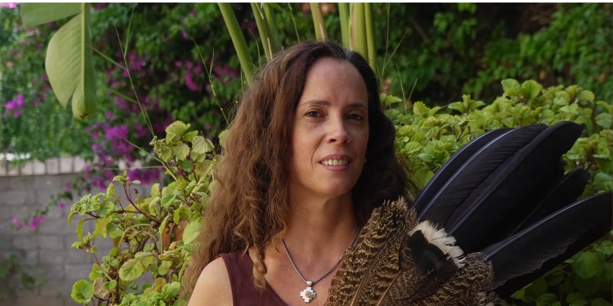 Woman with long hair holding a fan made of large feathers in a garden.
