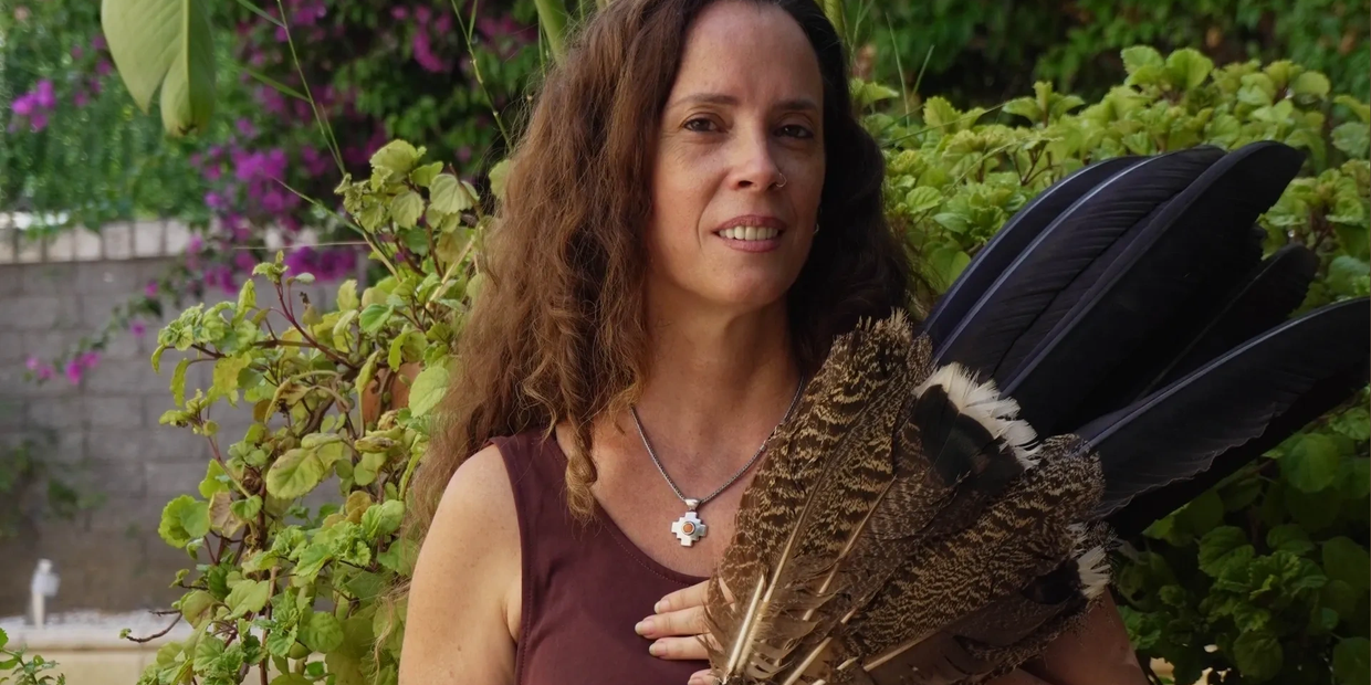 Woman with long hair holding a fan made of large feathers in a garden.