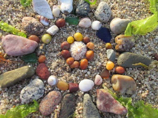 Mandala de piedras y conchas sobre arena.