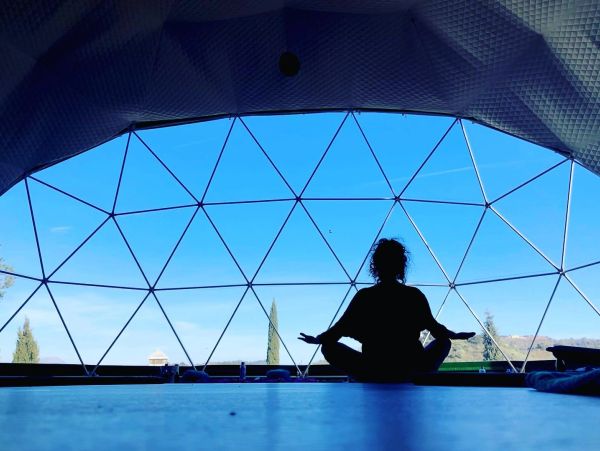 Persona meditando dentro de una estructura geodésica con vista al cielo.