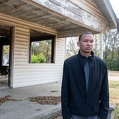Man standing outside a rundown house.