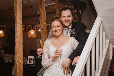 Newly wed couple holding champaign glasses smiling at the camera, captured by Kaos Photography Essex