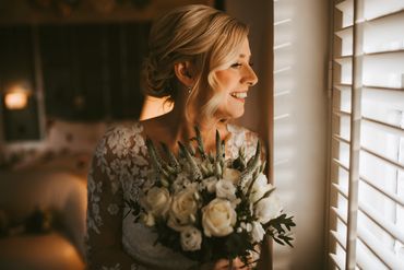 A smiling bride holding her flowers looking at the window at her guess arriving to Friern Manor 