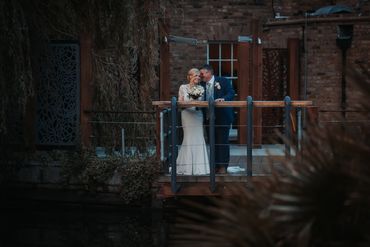 A newly wed couple standing on a bridge at Friern Manor with groom whispering in in brides ear 