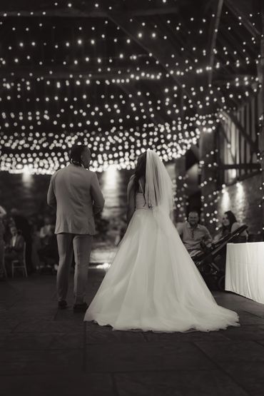 A black & image of a newlywed couple under a stream of fairy lights at cooling castle barn in Kent