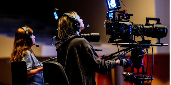 Dos personas operan cámaras y usan auriculares en una producción.
