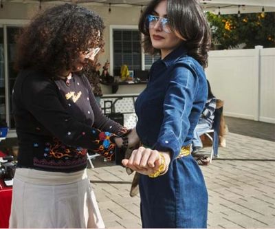 Two women holding hands outdoors, one in denim dress and sunglasses.