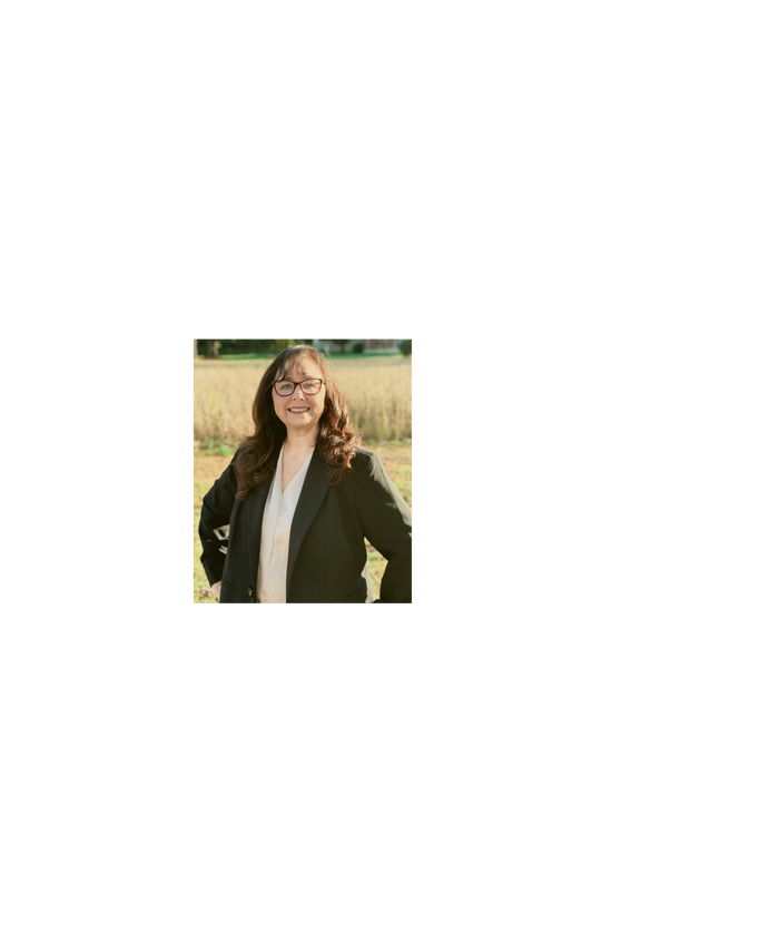 Smiling woman in glasses and a black blazer outdoors on a sunny day.