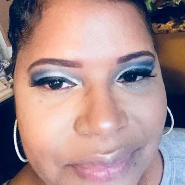 Close-up of a woman with bold blue eye makeup and hoop earrings.