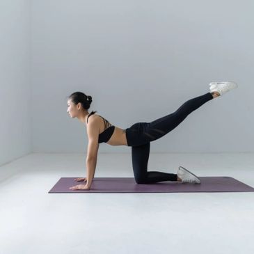 Woman practicing a leg lift yoga pose on a mat in a minimalist room.