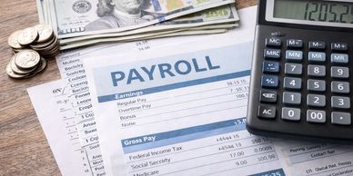 Payroll documents, money, and calculator on a wooden table.