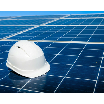 Engineer in safety gear by solar panels and wind turbines under clear blue sky.